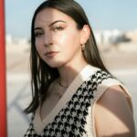 Outdoor portrait of a stylish young woman with gold jewelry in natural sunlight.